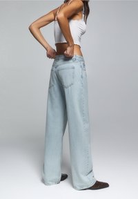 Jeans de mezclilla de pierna ancha en color azul claro. De tiro alto, con bolsillos traseros, bordes deshilachados y un ajuste relajado. Combinados con una blusa corta blanca.