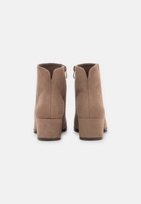 Brązowe zamszowe botki za kostkę na niskim słupku, z V-kształtnym wycięciem z tyłu i zamkami po obu stronach, co ułatwia zakładanie.