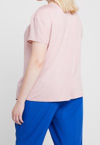Rosa kortärmad topp med en mjuk struktur, med en rundad halsringning och lös passform, i kombination med blå byxor.