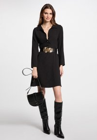 Vestito nero a maniche lunghe con colletto, caratterizzato da una cintura con dettaglio dorato. Abbinato a stivali neri al ginocchio e a una piccola borsa nera.
