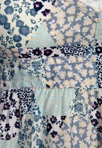 Mönstrad tyg med blommor och geometriska former i blått, krämfärgat och svart med samlade sömmar och mjuk textur.