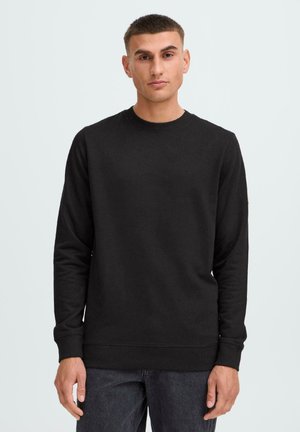 Musta collegepaita puuvilla-sekoitemateriaalista, pyöreä pääntie, pitkät hihat, ribbireunat hihansuissa ja helmassa, sileä pinta, minimalistinen muotoilu, ilman näkyviä logoja.