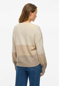 Sweter w paski w kolorze kremowym i beżowym, o luźnym kroju, opadających ramionach i ściągaczach. Miękka tekstura i swobodny fason.