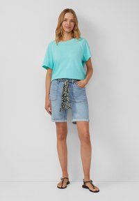 Turquoise t-shirt met korte mouwen en een losse pasvorm, gecombineerd met lichtblauwe denim shorts met een gestreepte zwart-witte strikriem. Zwarte sandalen.