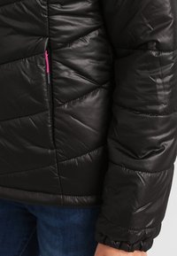 Černá polstrovaná bunda s prošívaným vzorem a texturovaným povrchem. Obsahuje zipovou kapsu s růžovým akcentem poblíž lemu.