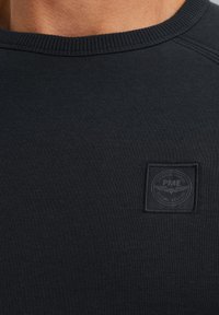 Zwarte sweatshirt met een ribgebreide kraag en een textuurstof. Bevat een klein, reliëf rechthoekig logo-opkraag op de borst.