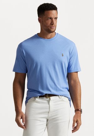 Tricou bleu deschis cu guler rotund, din material moale, având un mic logo brodat pe piept. Asortat cu pantaloni albi și o curea maro.
