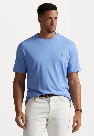 Lyseblå t-shirt med rund hals i blødt stof, med et lille broderet logo på brystet. Matchet med hvide bukser og et brunt bælte.