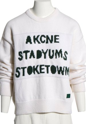 Pull tricoté blanc avec texte noir « AKCNE STADYUMS STOKETOWN » affiché à l'avant, porté sur un mannequin.