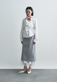 Balta pogām aiztaisāma krekla krekls ar zelta pogām, pelēka svārki ar mežģīņu apdari un balti, ar smailiem purngaliem ķēžu kurpes. Modele valkā rozā ar rakstu lakatu.