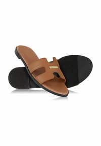 Brązowe skórzane sandały wsuwane z dwoma paskami i małym złotym akcentem. Czarna gumowa podeszwa z teksturowanym gripem dla stabilności.
