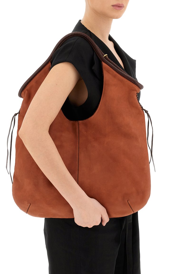 Borsa in suede marrone con una parte superiore curva, ampia apertura e dettagli con cordoncino. Texture liscia, design minimalista e forma semi-strutturata.