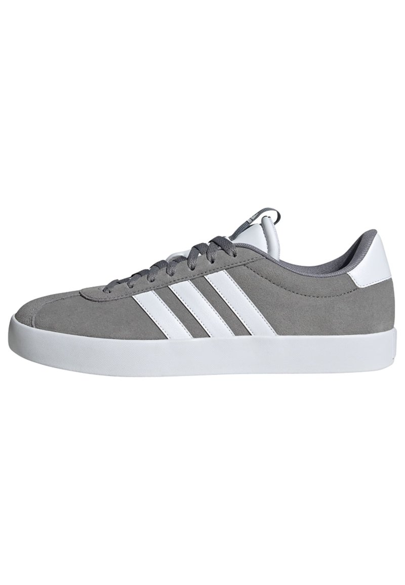 Zapatilla de ante gris con rayas blancas, punta redondeada, suela de goma y forro de tela. Presenta cordones gris y un lazo en el talón.