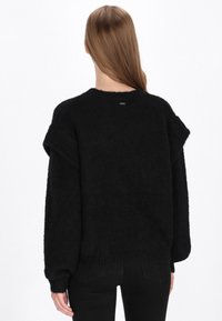 Sort oversized sweater med en tekstureret finish, dropped skuldre og en bred hals. Har en lav ribbede kant og et lille logo på bagsiden.