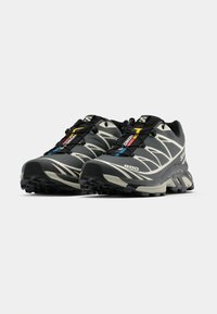 Fekete és szürke sportcipők texturált talppal, elegáns kialakítással, rugalmas fűzőkkel és színes díszítőelemekkel a nyelvén.