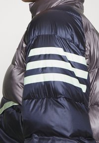 Padded jacket w ciemnym granacie i szarości o pikowanej fakturze. Posiada trzy jasnoszare paski na ramieniu oraz zamek błyskawiczny.