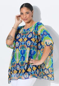 Blusa trasparente e colorata con un vivace motivo floreale nei colori blu, verde, giallo e rosso, con maniche larghe e ampie e scollatura tonda.