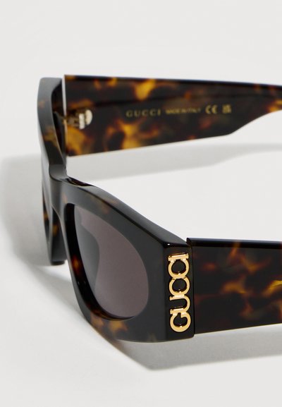 Γυαλιά ηλίου σε στυλ χελώνας με σκούρους φακούς, που διαθέτουν το χρυσό λογότυπο "GUCCI" στο μπράτσο και την επιγραφή "Made in Italy" στο εσωτερικό του βραχίονα.