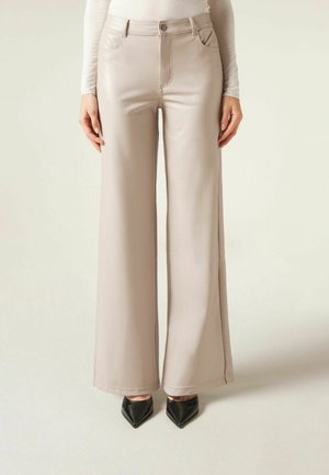 Pantaloni beige a vita alta e gamba larga indossati con una maglia a maniche lunghe color crema e décolleté nere con punta a punta.