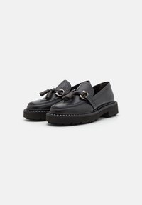 Mocassins en cuir noir avec des franges et des accents en métal. Semelle en caoutchouc épaisse avec un motif en zigzag. Design élégant et texture lisse.