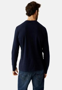 Marineblaues Langarm-T-Shirt mit Rundhalsausschnitt, aus weichem Stoff. Getragen mit blauen Jeans, zeigt ein einfaches Rücken-Design.