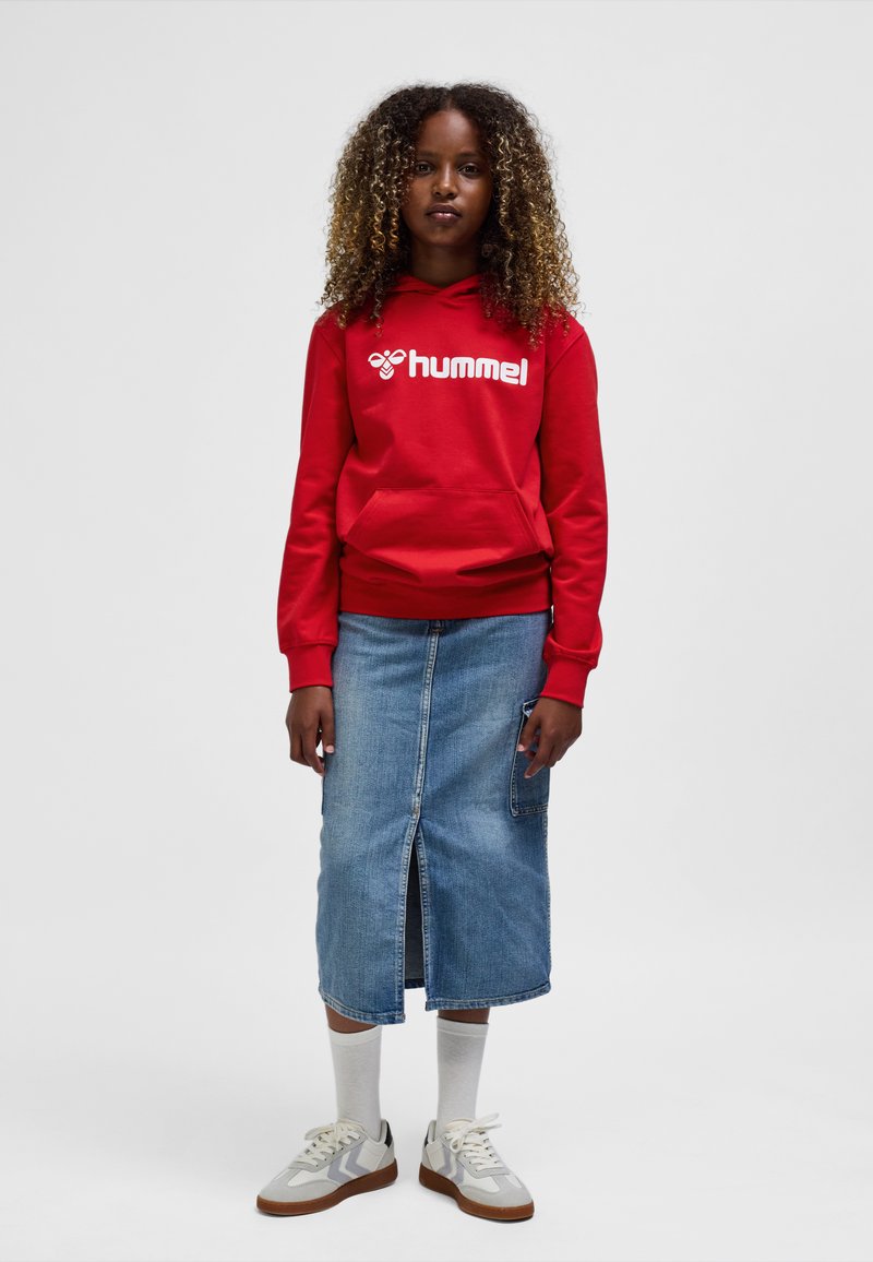 Roter Hoodie mit weißem "hummel"-Logo, blauer Jeansrock mit vorderlichem Schlitz und grauen Sneakern mit weißen und beigen Akzenten, kombiniert mit weißen Socken.