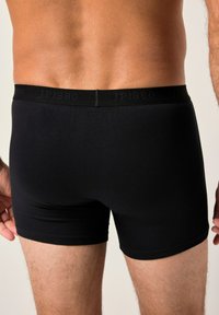 Bóxers de algodón negro con una suave cinturilla elástica que presenta una marca en relieve. Textura suave y diseño ajustado.