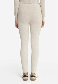 Leggings beiges en tissu doux avec une texture lisse. Design ajusté, longueur cheville, associés à des chaussures claires avec des accents noirs.