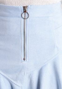 Vaaleansinihkö nobellikankainen hame, jossa on edessä vetoketju hopeisella vetotangolla, hienostunut paneelimuotoilu ja pehmeä textura.