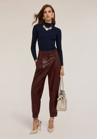 Maglione a costine blu navy, pantaloni plissettati in ecopelle bordeaux, borsa beige e tacchi nudi. Collana e orecchini statement in oro.