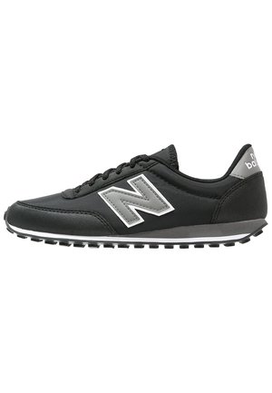Sort New Balance sneaker med gråt logo, hvid sålstribe, snøredesign og tekstureret gummiydersål, set fra siden.