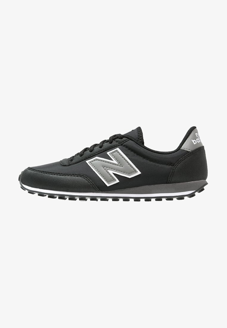 Basket New Balance noire avec logo gris, bande blanche sur la semelle, design à lacets et semelle extérieure en caoutchouc texturé, vue de côté.