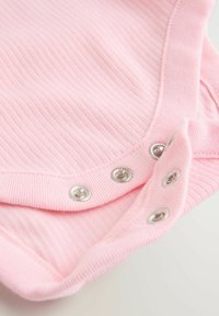 Rožnata rebrasta tkanina z gladko teksturo, s kovinskimi pritiskači. Zapiranje na dnu in zaobljen izrez na vratu.