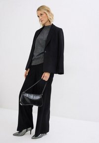 Blazer nero con chiusura a bottone, top grigio strutturato, pantaloni neri a gamba larga, borsa nera in vernice e décolleté metallici con punta. 