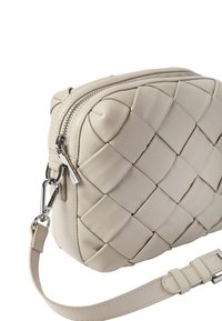 Beige leren crossbodytas met een geweven patroon, afgeronde vorm, zilverkleurige details en een verstelbare riem. Voorzien van een ritssluiting aan de bovenkant.
