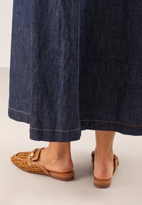 Falda de mezclilla con un lavado azul oscuro y costuras visibles, combinada con zapatos de lona trenzados en tono beige con suela plana y detalle de hebilla decorativa.