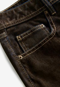 Mørkebrune denimjeans med kontrastfarvet gyldent syning. Har en lille frontlomme med metalnitter og en synlig talje.