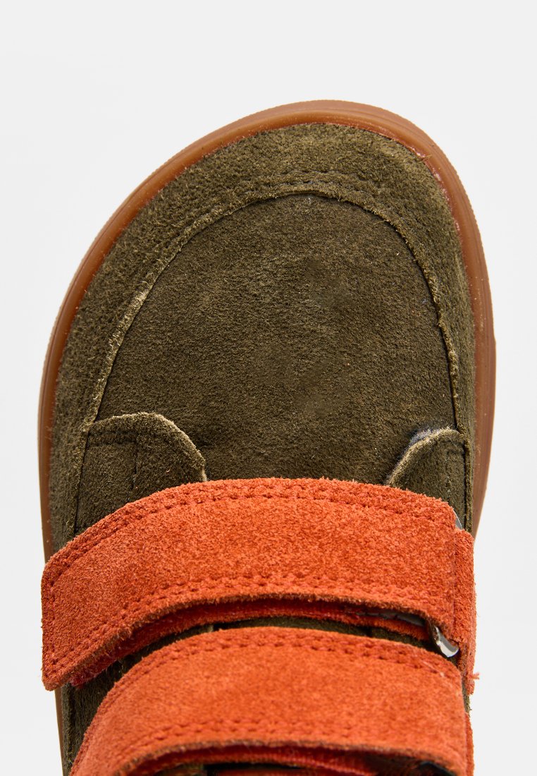 Zapato de ante marrón con una correa de velcro naranja, diseño de punta redonda, parte superior texturizada y suela de goma, visto desde arriba.