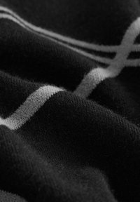 Tissu noir avec des lignes blanches entrecroisées formant un motif en grille, montré en gros plan avec une texture et des plis visibles.