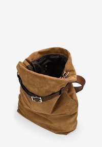 Bolso de ante marrón con una textura suave, una correa de cuero marrón ajustable y una apertura superior con cremallera que revela un forro interno oscuro.