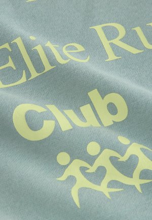 Világos kék anyag, amelyen nagy sárga felirat olvasható: "Elite Run Club", valamint stilizált grafika látható, amely futás közben lévő alakokat ábrázol. Simított felület.