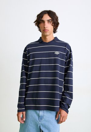 Polo shirt à manches longues bleu marine avec des rayures horizontales blanches, col côtelé et logo brodé sur la poitrine gauche. Tissu en coton, coupe décontractée.