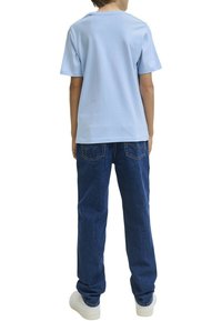 Camiseta de manga corta azul claro, corte relajado, combinada con jeans de mezclilla azul oscuro. Estilo casual, con un mínimo de detalles en la tela y la costura.