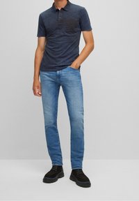 Tmavě modré polo tričko s krátkými rukávy a kapsou, doplněné světle modrými džínami a černými šněrovacími botami, se střihem rovného střihu nohavic.