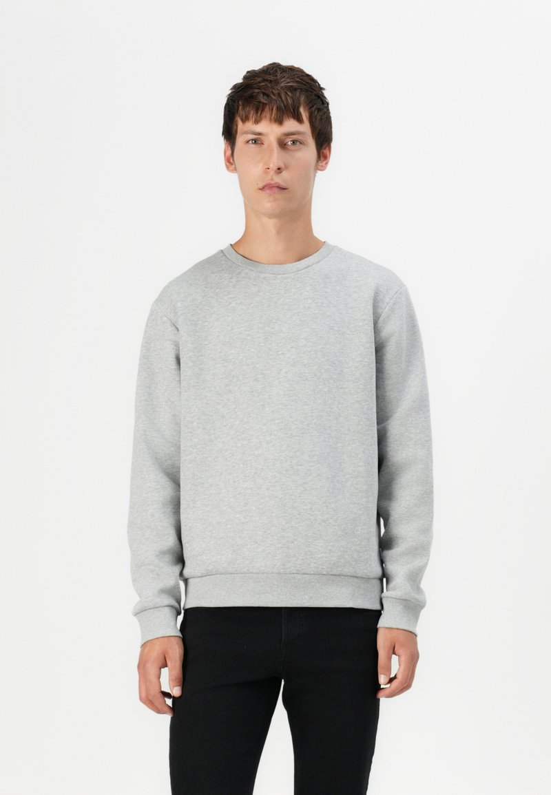 Grå hettegenser med rund hals, ribbede ermer og kant. Myk, glatt tekstur og avslappet passform, kombinert med tettsittende svarte jeans.