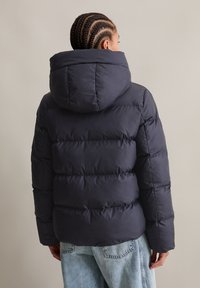 Dark navy puffer jacket with a large hood, featuring horizontal quilted sections and a soft, smooth texture. Back view shows relaxed fit.