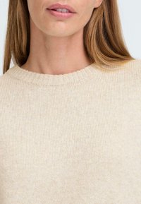 Pull en maille beige clair avec une texture côtelée, doté d'un col rond et de petites nuances. Tissu lisse au fini doux.