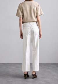 Camiseta de algodón beige, de corte relajado, combinada con jeans de pierna ancha blancos de tiro alto con bajos deshilachados. Tacones marrones completan el conjunto.