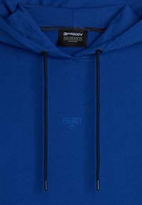 Sweat à capuche bleu avec une texture lisse, doté de cordons de serrage noirs et d'un logo de marque subtil imprimé à l'avant.