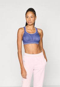 Μωβ αθλητικό σουτιέν με διαμορφωμένα μπούστα, φαρδιές τιράντες και αντίθετη ροζ επένδυση. Λεία υφή, εφαρμοστό σχέδιο, σε συνδυασμό με ροζ φόρμες.